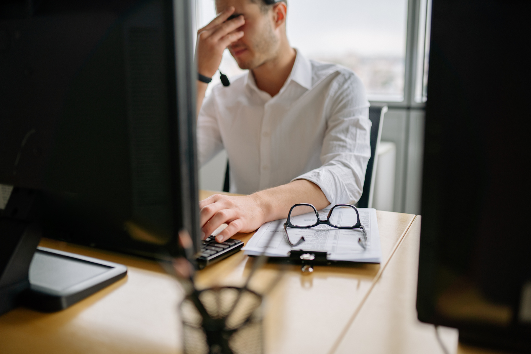 Frustrated operator at a desk between two monitors, head in hand